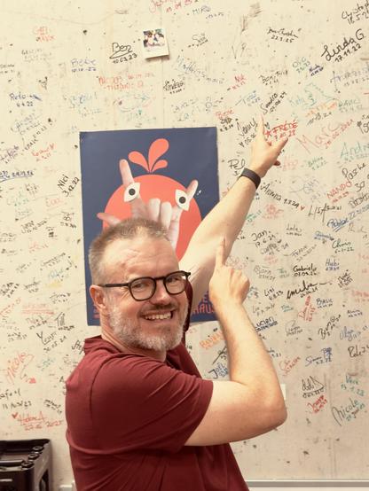 Ich stehe vor einer Wand voller Unterschriften und zeige auf meine