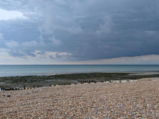 Dark bank of cloud extends over the sea creating a lovely dark horizon. The pebble beach at low tide in the foreground.