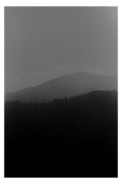A grainy black and white photograph of distant mountain ridges fading into mist. The dark silhouette of the foreground hills contrasts with the lighter tones of the background, evoking a quiet, contemplative mood. A minimal landscape for #SilenceSunday.