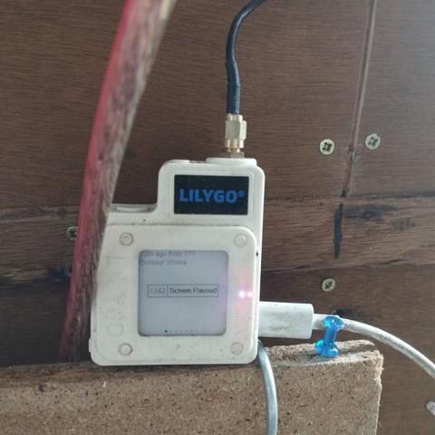 techo de lilygo posé sur le haut de mon panneau électrique dont on ne voit que les 3 derniers centimètres, un cable usb-c branché pour le charger et un coax le relie à une antenne qui est hors cadre. l'appareilqest blanc, le logo bleu sur fond noir. sur l'écran e-ink se trouve le message salut Shinra, le nom court du noeud c242 et rcreen paused