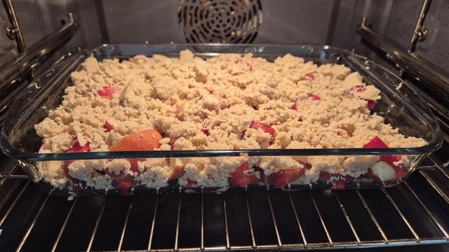 Gezuckerte Pfirsiche in Stücken in Auflaufform aus Glas, mit Streusel bedeckt und im Ofen