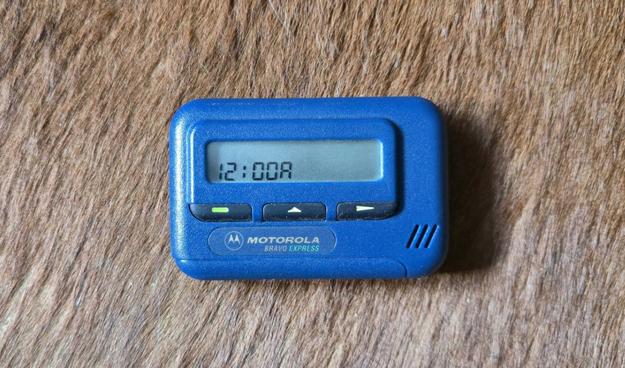 Blue Motorola Bravo Express pager with three buttons, showing "12:00A" on the screen