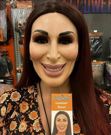 A woman with long brown hair wearing a Halloween mask that's all uncanny valley because it looks just like Laura Loomer. The tag, still attached, rads "Loomer Goon."