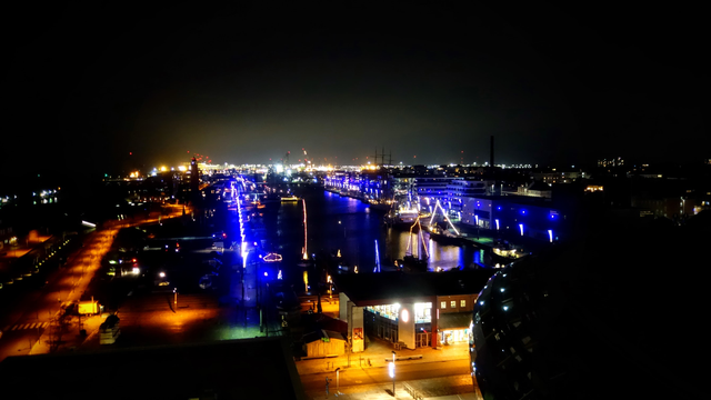 Blick bei Nacht auf den Innenhafen von Bremerhafen. Die Lichter schimmern gelb und blau. In der Ferne glüht die helle Beleuchtung des Containerterminals.
