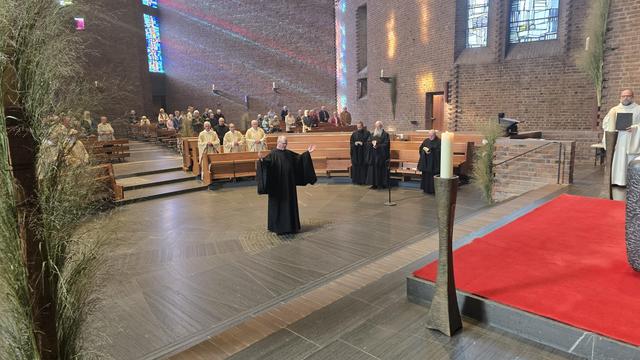 P. Karl steht mit erhobenen Händen in der Mitte der Kirche und singt den Professgesang.