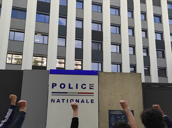 photo de poings levés devant un panneau "Police nationale" du commissariat de Lyon 8