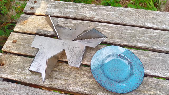 Une fois plié, la pièce devient un support pour émailler. Il est posé à côté d'une coupelle émaillée en bleu.