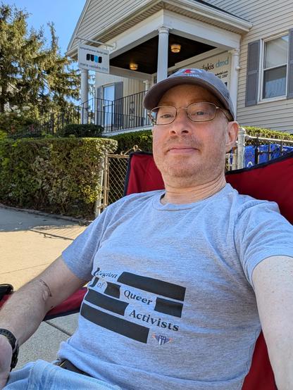 Outdoor selfie, seated, house in the background, wearing "Legion of queer activists" shirt
