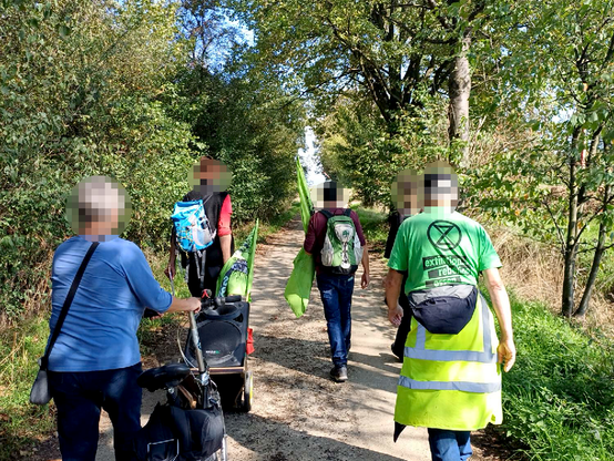 Spaziergänger*innen auf einem Waldweg tragen grüne Fahnen ("Hambacher Forst bleibt")