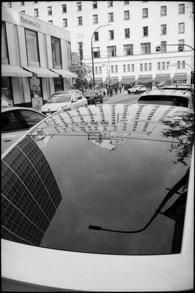 A hotel is reflected in the curved roof of a parked car.