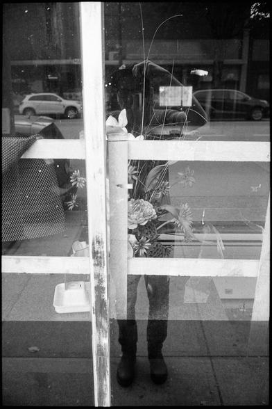 The photographer captures his reflection in a storefront floral arrangement.
