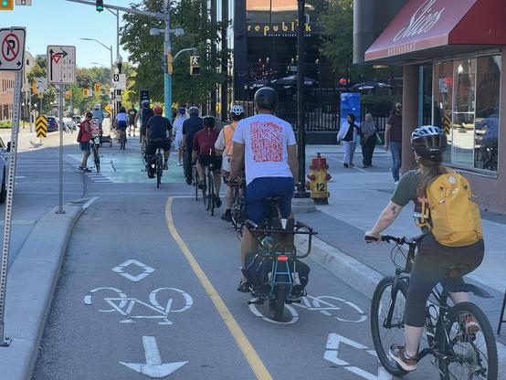 An urban intersection has many cyclists passing through a green light, riding on a separated bike path.