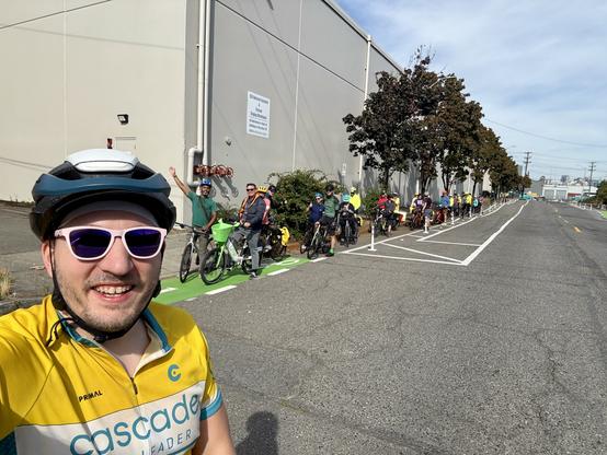 Selfie in my yellow Cascade Ride Leader jersey in front of a large group of cyclists in the new 6th Avenue protected bike lanes in SODO