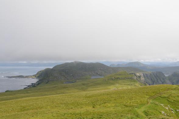 A photo of a green hilly landscape with jagged coasts. The sky is a solid wall of white cloud.