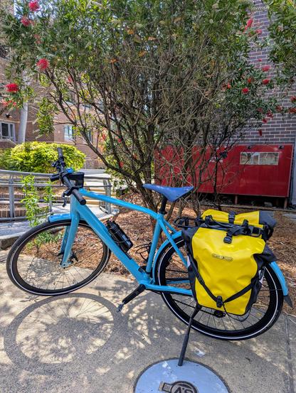 Photo of a blue Orbea Vibe ebike with pannier bags, parked on a pavement.