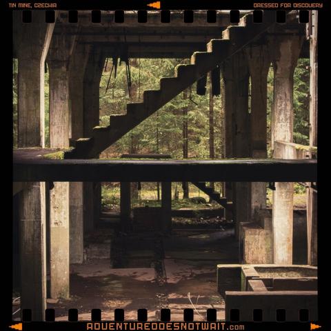 A moody photograph of the abandoned Rolava Tin Mine in Czechia, featuring a moss-covered staircase framed by concrete pillars, inspiring rugged organic cotton adventure apparel.