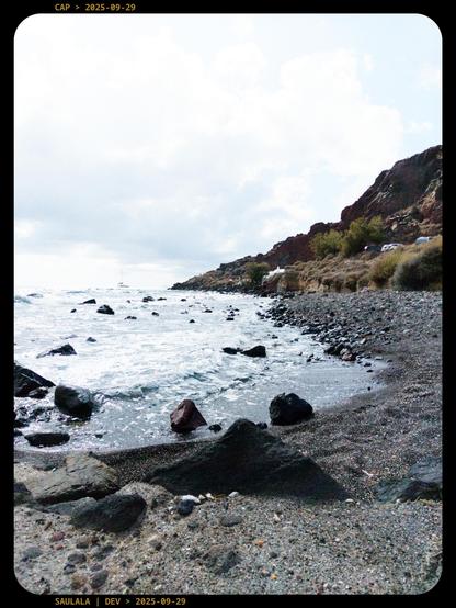 Une plage de cailloux sous un soleil dardant ses rayons à travers une voûte de nuages en arrière plan. La mer semble rejoindre le ciel.