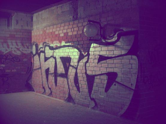 Großes Graffito »Intus«, in eine dunkle Ecke der Ruine des Ihmezentrums in Hannover-Linden gesprüht, bei Nacht aufgenommen. Trotz der Dunkelheit deutlich erkennbar: Die kaputte Laterne darüber.