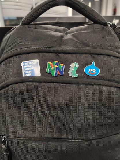 A black backpack with a pin of a Final Fantasy selection menu, a Nintendo 64 logo, a Grub from Hollow Knight and a Slime from Dragon Quest
