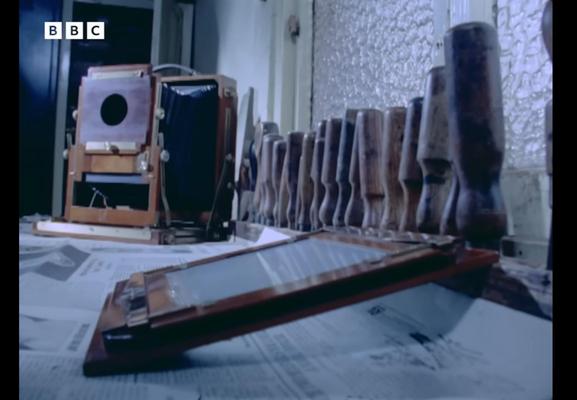 A scene in an old workshop with a partly finished camera body and  of chisels lined up along the wall.