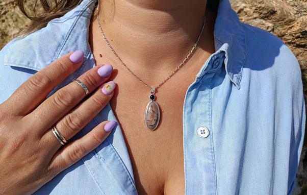 a pendant with silver chain. in has two gemstones one small round black colored and a bigger one oval shaped pink with black lines. it's worn on a woman's boost