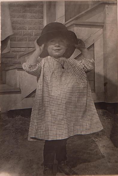 Little girl in a gingham plaid dress wearing a man's bowler hat