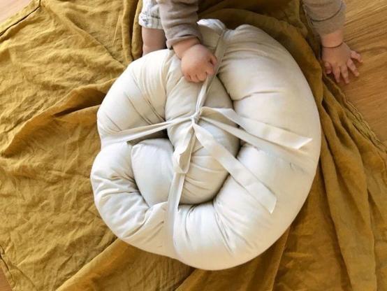 Toddler's hands holding a coiled Oolie bolster pillow in organic cotton, on top of a mustard yellow fabric.