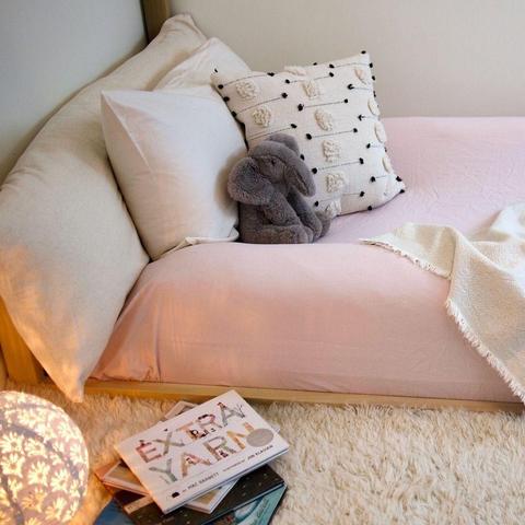 Oolie organic bolster installed on a toddler floor bed, tucked under the fitted sheet.