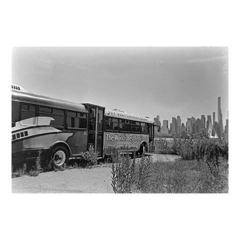 A NY Waterway bus sits in a vacant lot overlooking New York City skyline. The bus has the tag “The World’s Best Ferry”.