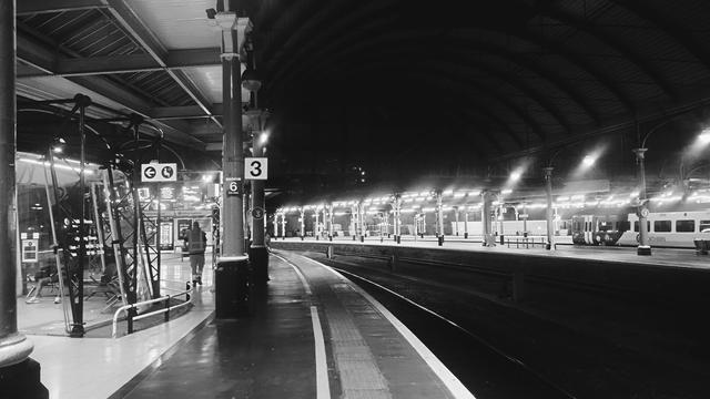 Looking along a long, curved platform at night in a large, Victorian railway station