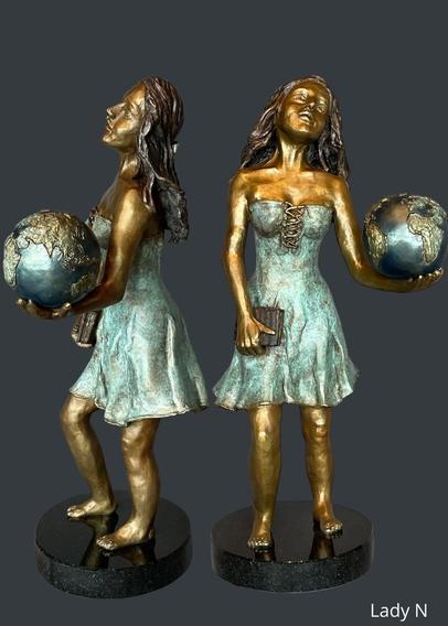 Une dame tient un globe terrestre dans sa main gauche et dans sa droite un livre. Il s'agit d'une sculpture en bronze.
