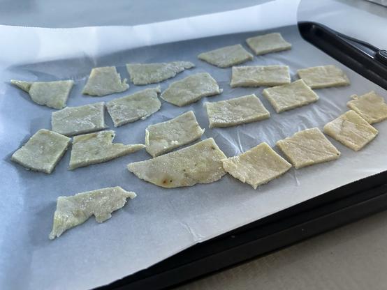Pieces of dough arranged on a parchment-lined baking tray, ready for baking. The shapes vary, with some resembling triangles and others rectangular.