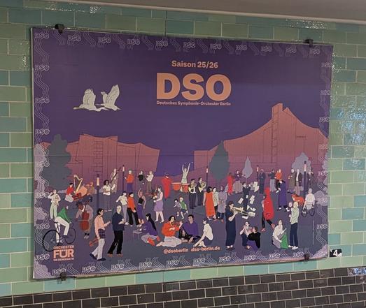 Das Bild zeigt ein großes, farbenfrohes Plakat an einer Wand mit grünlichen Fliesen. Das Plakat ist für die Saison 25/26 des Deutschen Symphonie-Orchesters Berlin (DSO) und zeigt eine lebendige Szene mit vielen Menschen, die Musik machen, tanzen und sich unterhalten. Im Hintergrund sind stilisierte Gebäude und zwei weiße Vögel zu sehen. Der Text "DSO" und "Deutsches Symphonie-Orchester Berlin" ist prominent dargestellt. Am unteren Rand des Plakats steht "Orchester für die Demokratie" und die Social-Media-Information "[@]dsob Berlin diso-berlin.de".