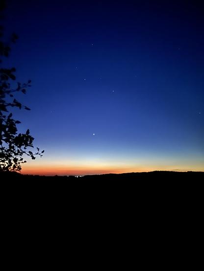 To my eyes, it’s quite dark. But the photo came up a bit brighter in the photo. It shows a deep blue sky with stars in it., It shows orange at the horizon above the hills, which appear totally black. You can see the lights of Alliston in a dip in the hills. It’s too early for the birds, it might be too early for me.