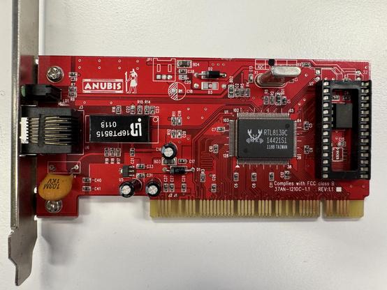 Realtek-based 32-bit PCI network card of the brand "Anubis". Red PCB with "Anubis" and an illustration of the Egyptian god etched in.