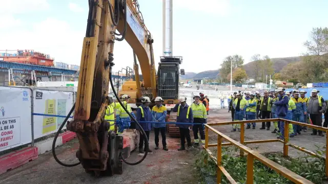 Large group of Tata Steel executives and contractors in yellow hi‑vis at Port Talbot steelworks, standing by construction equipment during the pickle line groundbreaking.