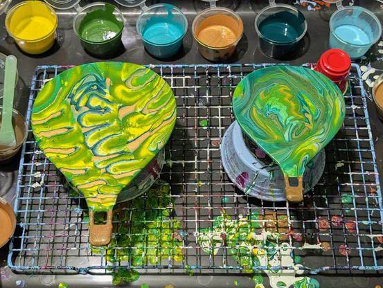 Two hot-air-balloon-shaped wooden cutouts decorated using fluid art; the colors used include gold, light blue, turquoise, a few shades of green, and a yellow.