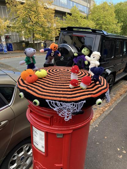 A red post box with knitted Halloween figures attached to its top.