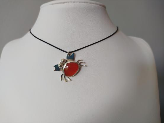 a silver pendant in shape of crab with an orange gemstone. it has a black nylon cord.