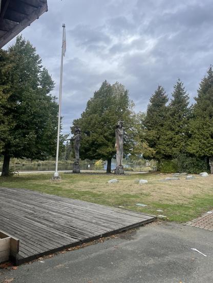 The flag for hupacasath flies atop a pole near the welcoming statues in a small park