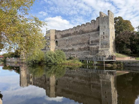 A castle. Reflected in a river below it. Blue sky above.
