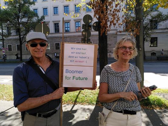 Eine weibliche und eine männliche Person aus der "Boomer-Genaration" zeigen die Rückseite vom Schild: "Wir sind hier, wir sind laut, denn wir haben's mit versaut. Boomer for Future"