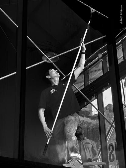 A window washer inside an industrial building holding a long-handled squeegee aloft in a pseudo-classical pose.