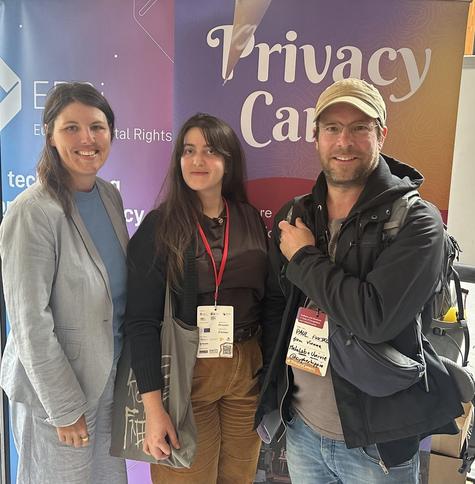 Three people stabding in front of a roll up with privacy camp writen on it.