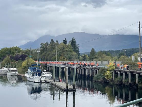 A line of people in orange shirts crosses a bridge