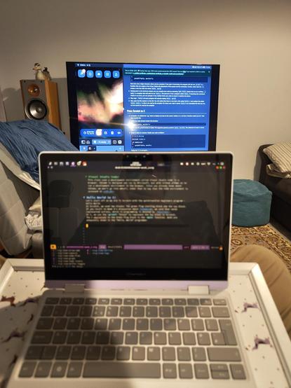 My Framework Laptop 12 computer sitting on my lap running Emacs Org Roam for my notes, in the background my TV showing CS50 notes and lofigirl on a split screen. 

In the midground, glothes sit on the back of the chair.