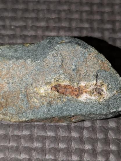 greyish pebble with a fractured surface revealing a little pocket, filled partly with some green mineral