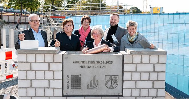Gruppenbild der Grundsteinlegung in Paderborn. Sechs Personen mit Maurerkellen in der Hand stehen hinter einer gemauerten Stele beim Herablassen der Zeitkapsel.