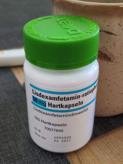 Kleine weiße Pillendose mit grünem Deckel. Sie enthält laut Aufschrift 100 Stück 50mg-Hartkapseln Lisfexamfetamin von Ratiopharm.