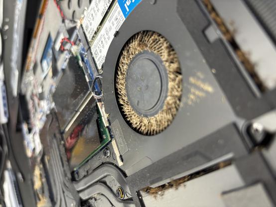 Primer plano de los ventiladores de un portátil obstruidos por polvo y suciedad, mostrando cómo la falta de limpieza afecta al flujo de aire y al rendimiento del equipo.